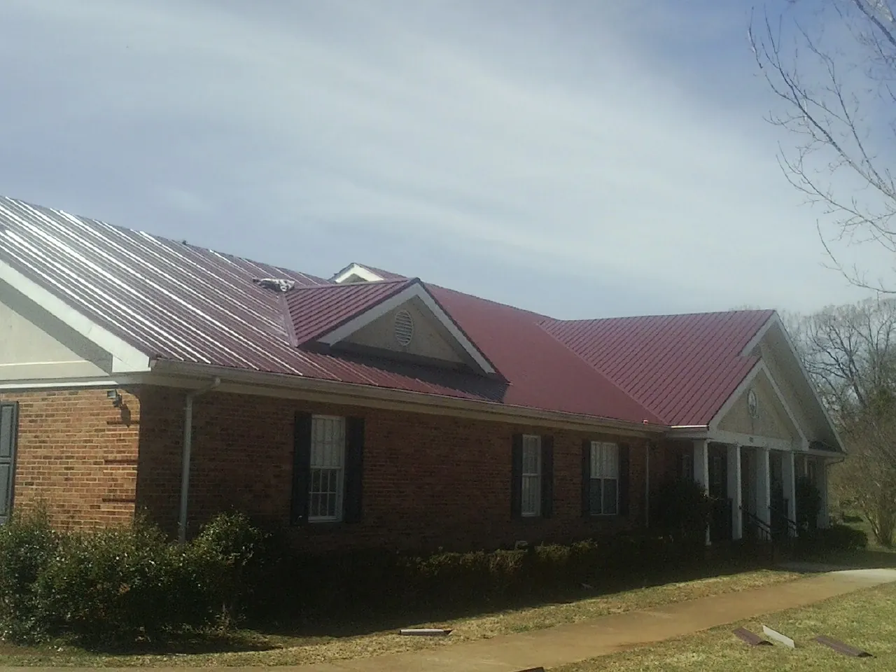 Red metal roof with gabled entries on a long brick building, from a Hail Damage Roof Repair job in Navarre