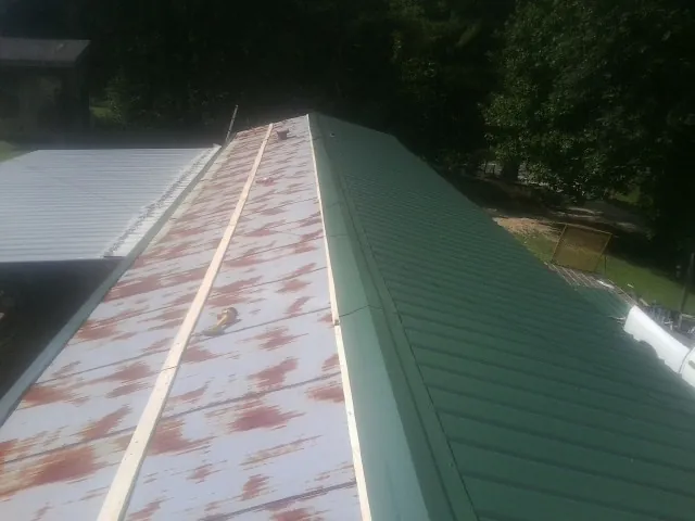 Old rusted panels beside newly installed green metal roofing — Wind Damage Roof Repair by Roofing Brothers in Navarre