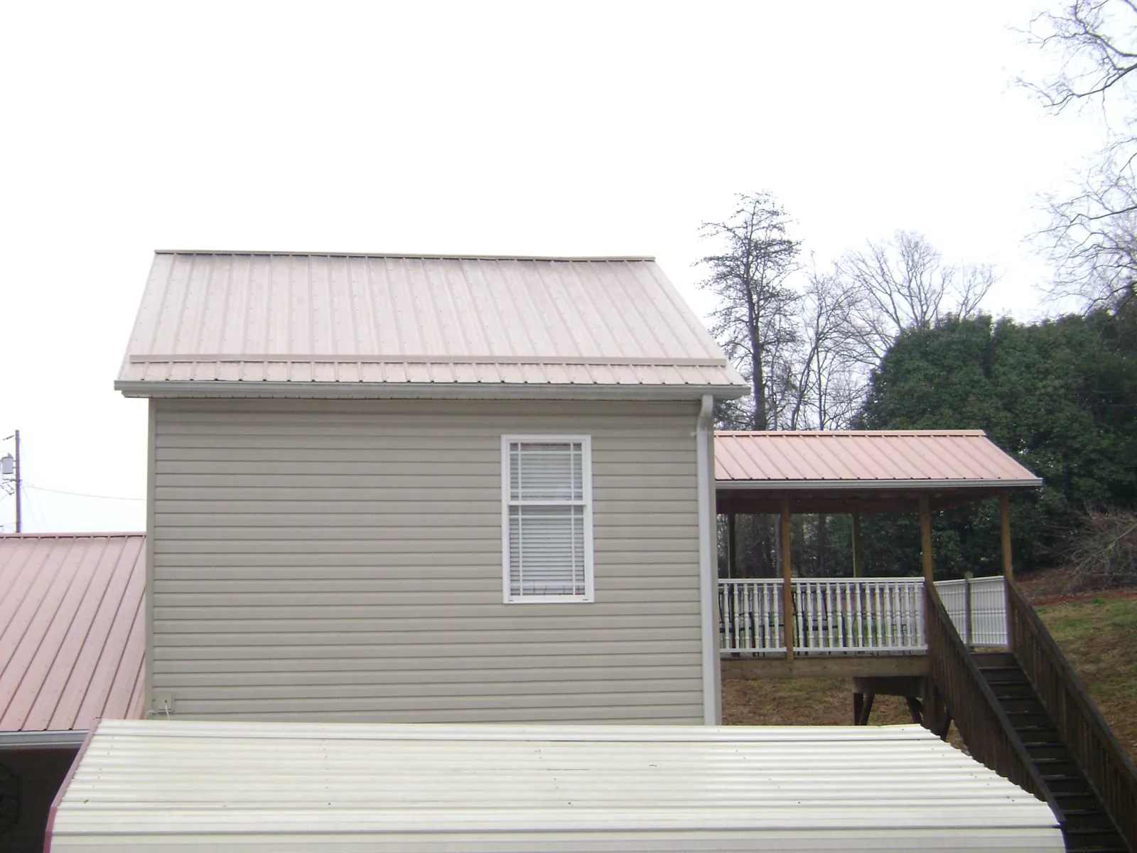 Tan metal roofs on a two story addition and attached porch, from a Roof Replacement job in Navarre